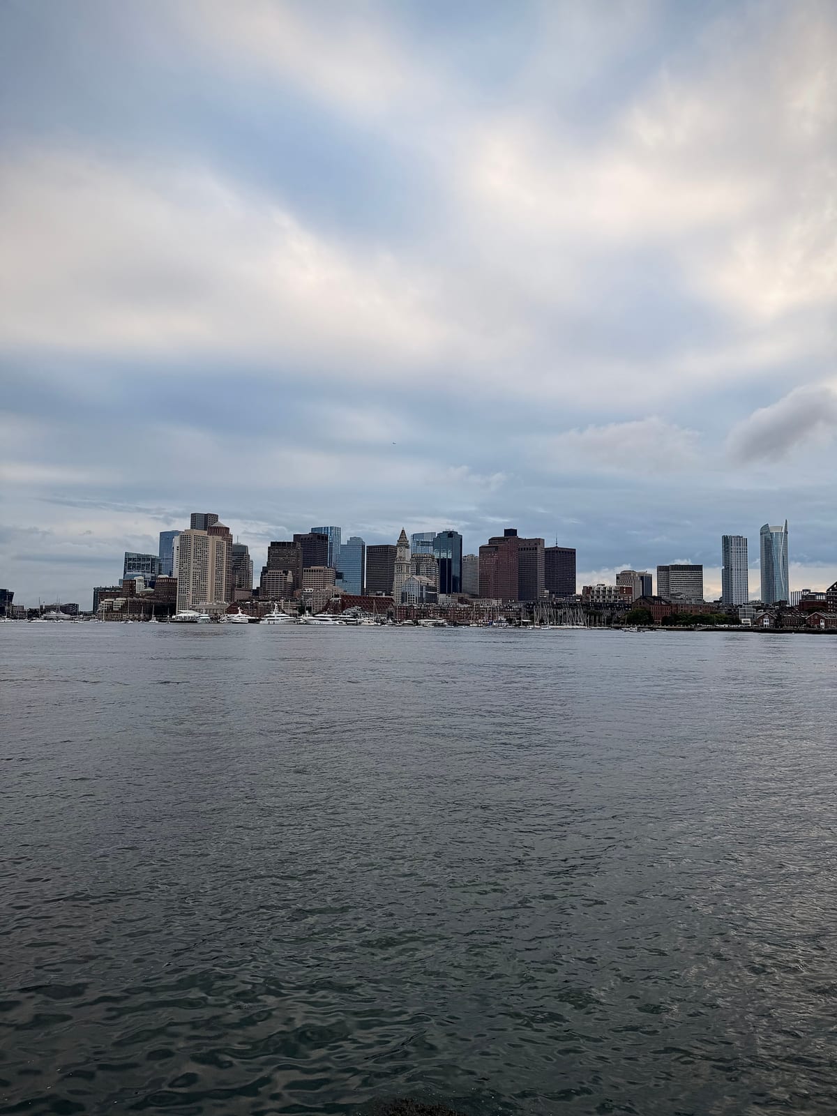 Boston's downtown skyline across the harbor beneath layers of gray clouds