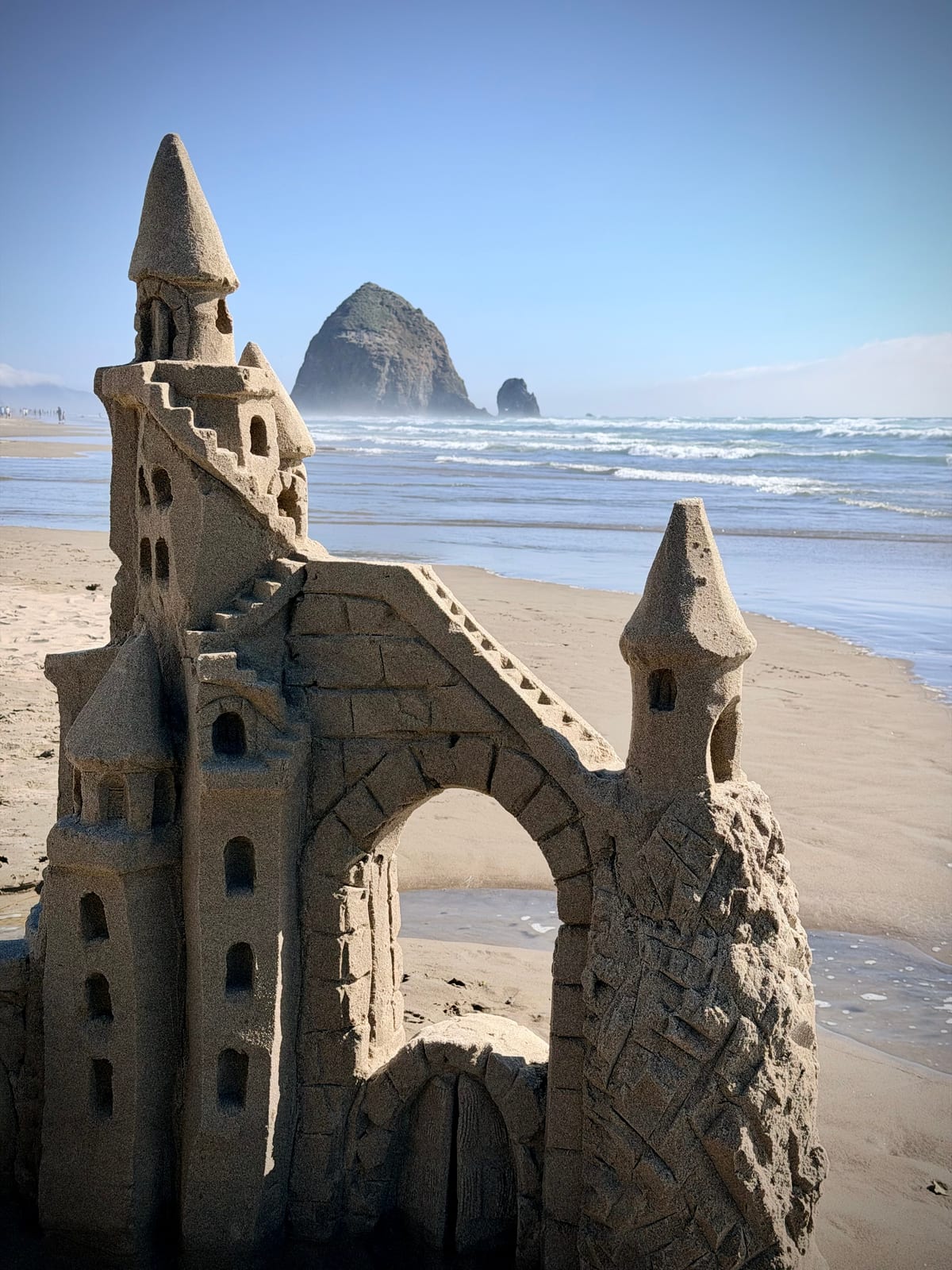An elaborate sandcastle on Cannon Beach with Haystack Rock rising behind it