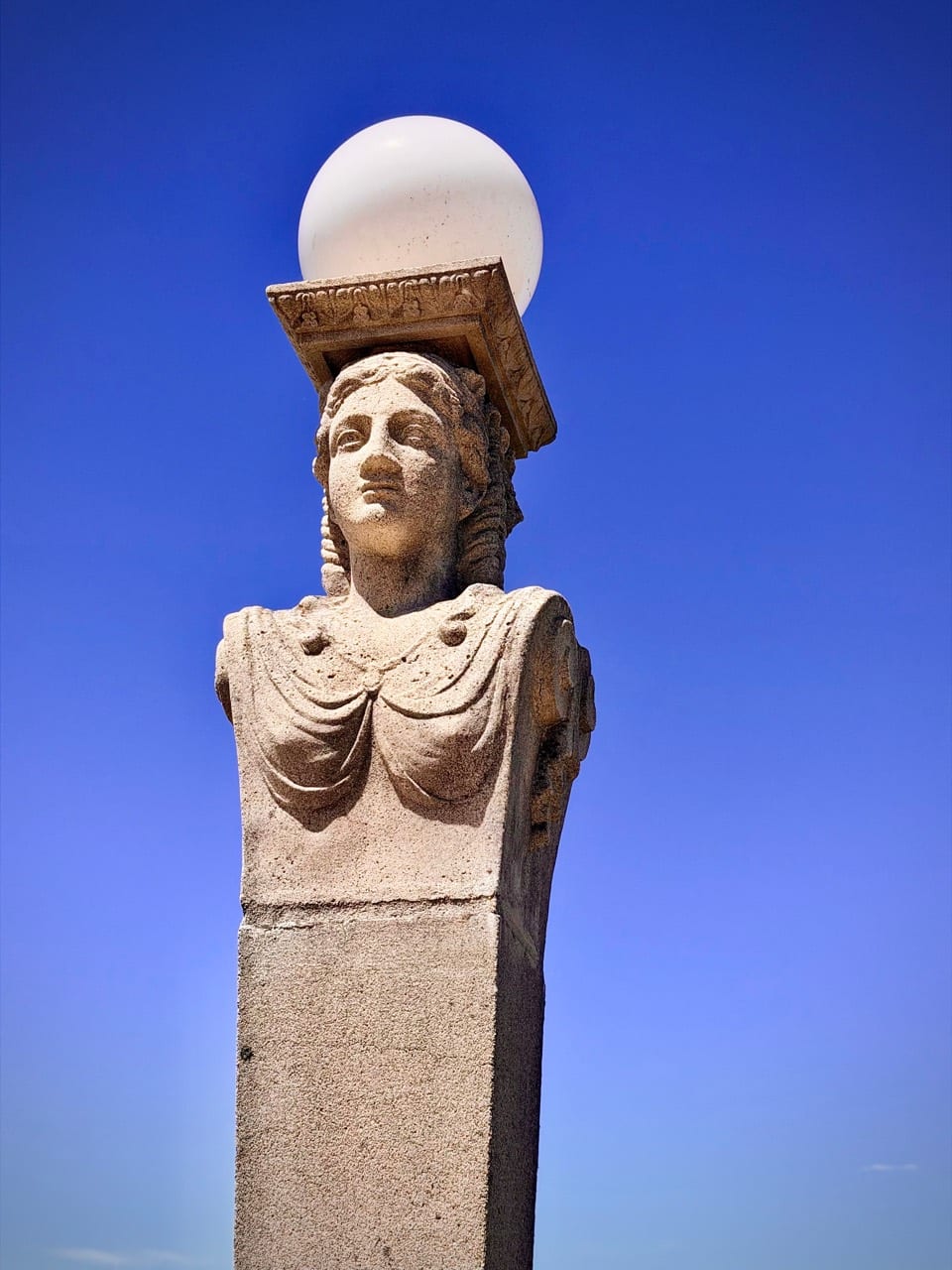A carved stone figure holding a globe lamp against a deep blue sky
