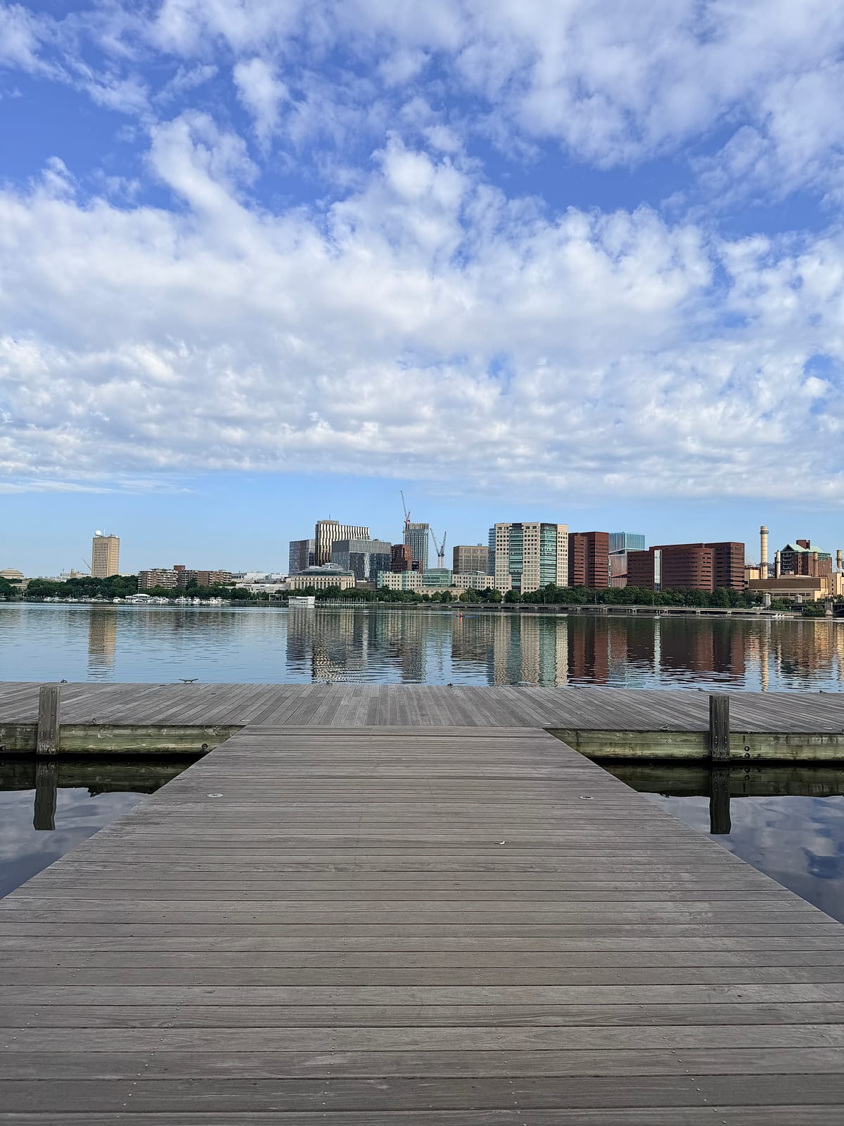 A wooden dock reaching toward the calm Charles River with the Cambridge skyline reflected in the water