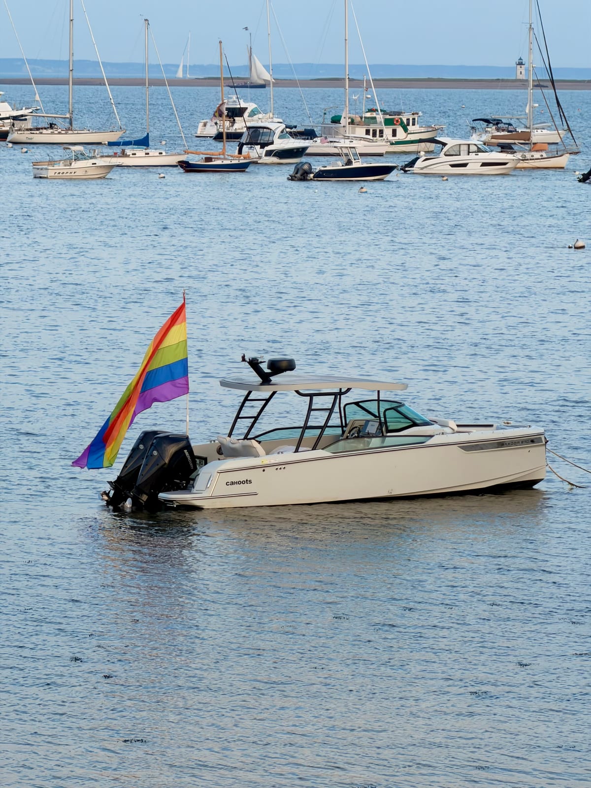 A motorboat named Cahoots flying a rainbow flag in Provincetown Harbor