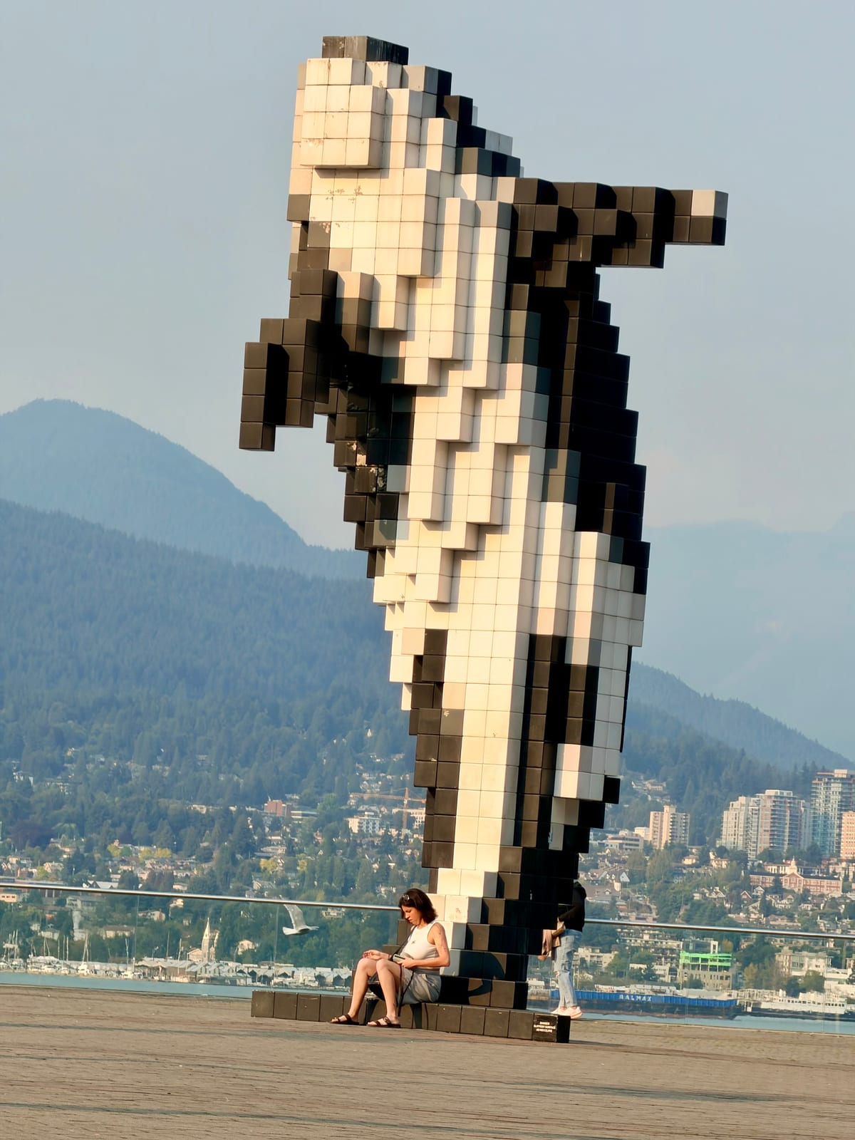 The pixelated Digital Orca sculpture with mountains and Vancouver behind it