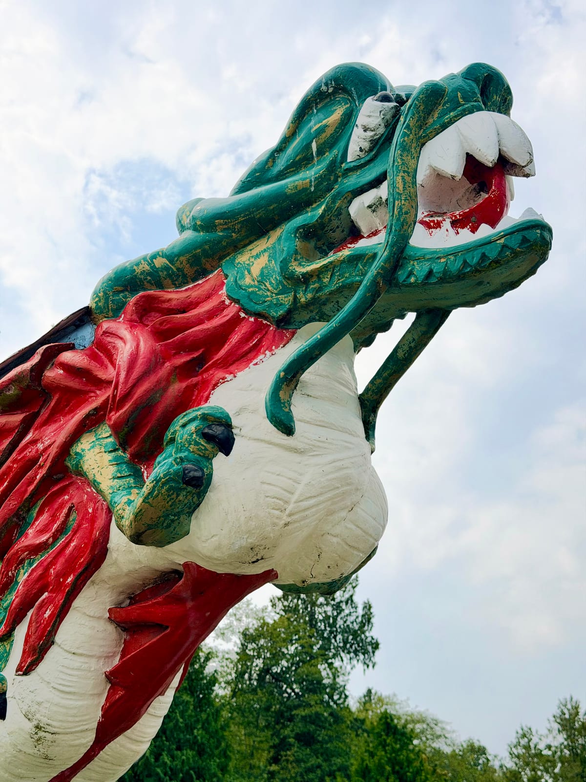 A weathered green, red, and white dragon figurehead against the sky