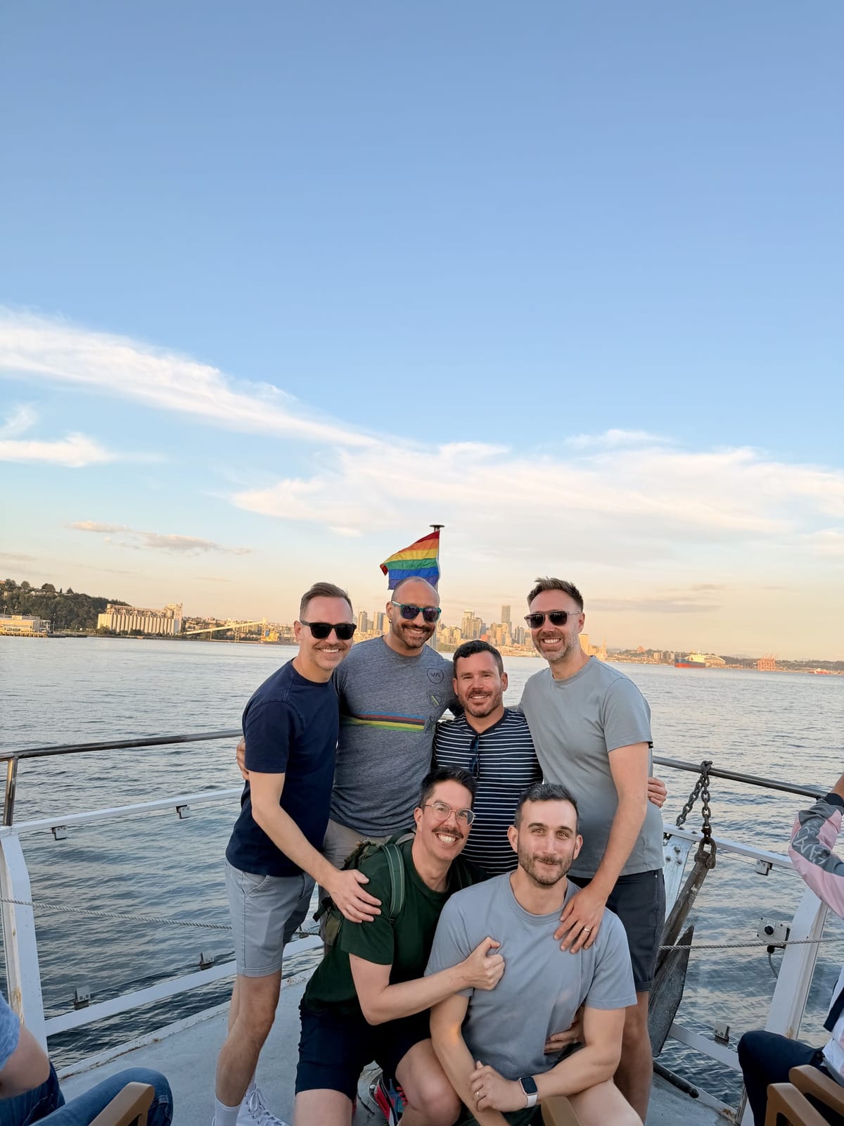 Six friends smiling on a harbor tour boat with the Seattle skyline and a Pride flag behind them