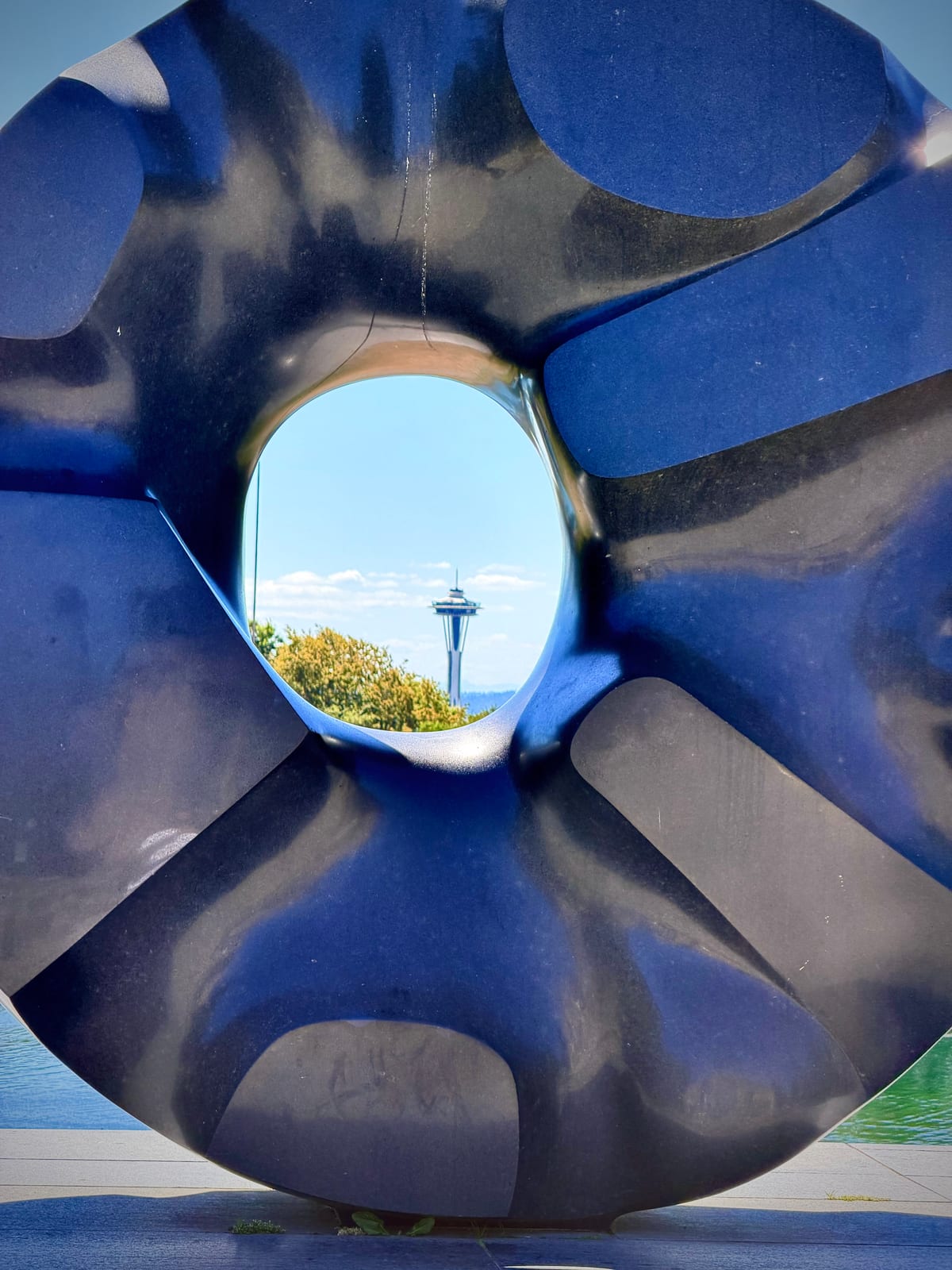 The Space Needle framed through the center opening of a large dark blue abstract sculpture in Volunteer Park