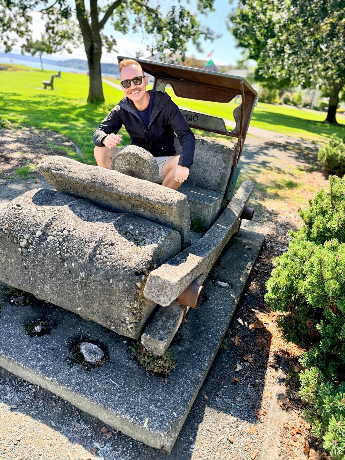 SML smiling reluctantly from the seat of a homemade stone Flintstones-style car in an Oak Harbor park