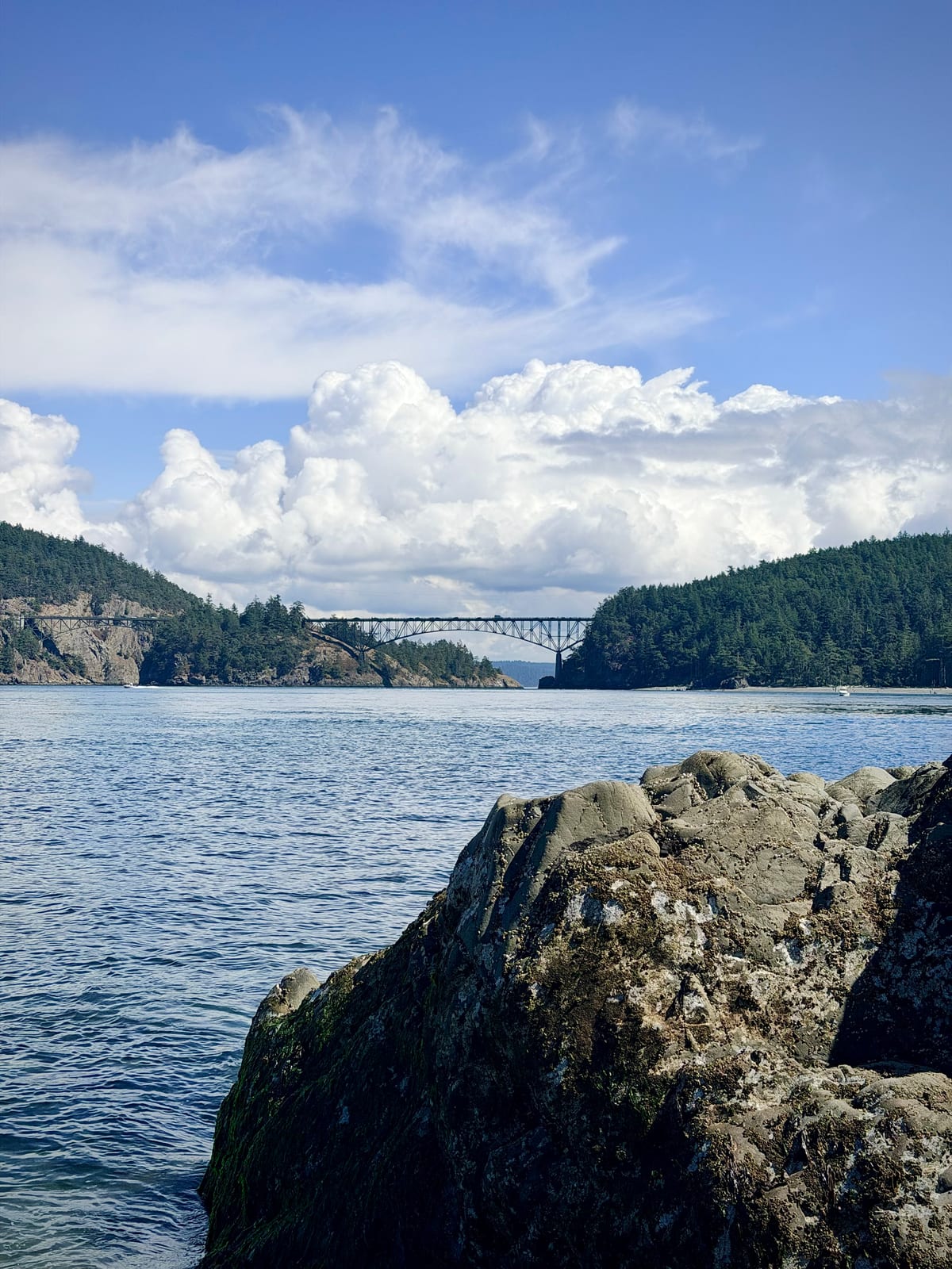 Deception Pass Bridge spanning two forested islands beyond a rocky shoreline