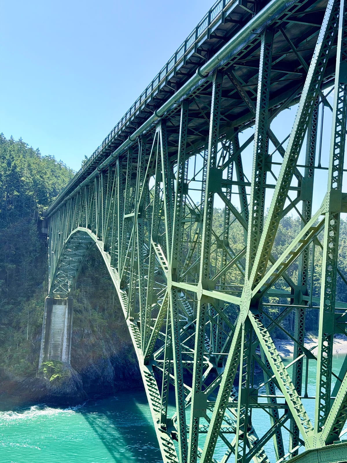 The green steel framework of Deception Pass Bridge arching over turquoise water